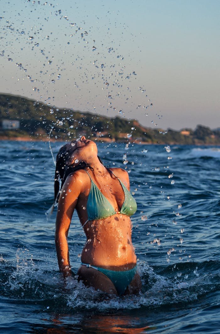 A woman in a bikini enjoying the ocean waves at sunset, creating a vibrant splash.
